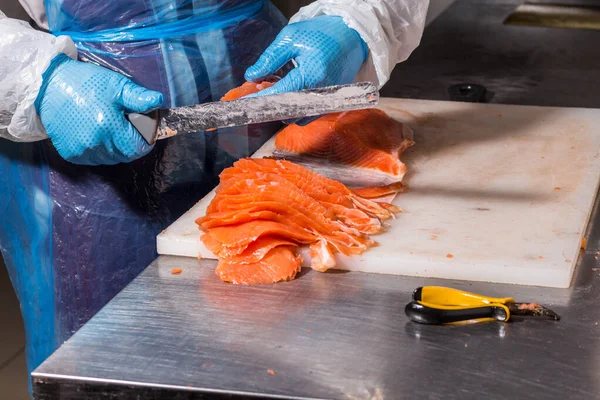 Producción de pescado. Worker corta pescado con un cuchillo en trozos para envasar Imágenes De Stock Sin Royalties Gratis