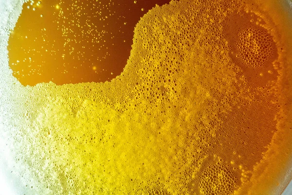 Espuma de cerveja com bolhas em um copo na luz de fundo. Na abordagem — Fotografia de Stock