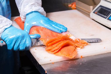 Fish production. Worker cuts fish with a knife into pieces for packaging clipart