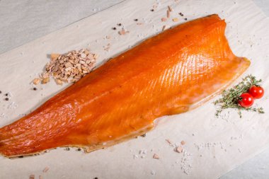 Tütsülenmiş kırmızı balık tütsülenmiş talaş ve tuzlu domateslerin yanında yatar. Durgun hayat