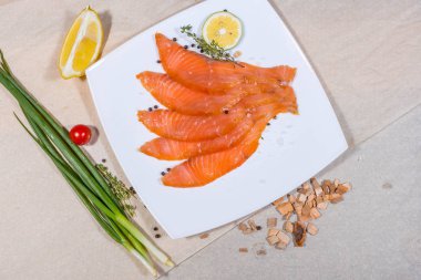 Dilimlenmiş kırmızı balık beyaz bir tabakta yatıyor. Sebzeler ve kıymıklar