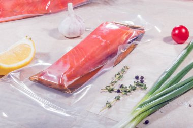 Kapalı bir vakum poşetindeki kırmızı balık bir yığın paketin arka planında. Tamamlanmış ürün