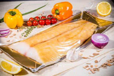 Mühürlü vakumlu beyaz füme balık arka planda sebze ve meyve limon biberi ambalajı