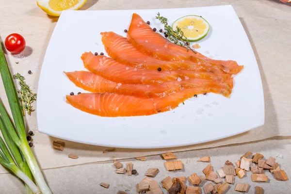 Červené ryby nakrájené na plátky leží na bílém talíři. Kolem zeleniny a třísek Stock Snímky