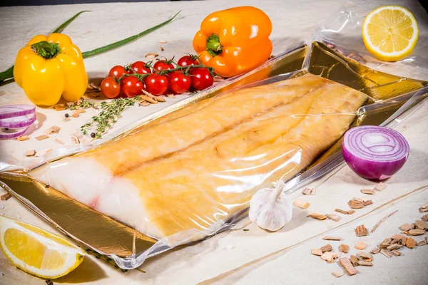 野菜や果物のレモンペッパーを背景に密封された真空包装で白い燻製魚 ストック写真
