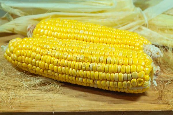 Kawałek kukurydzy obrane na drewnianej planszy na tle liści. Dwa kawałki. — Zdjęcie stockowe