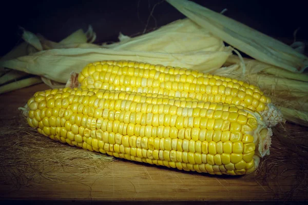 Кукуруза, очищенная на деревянной доске на фоне листьев. Виньет — стоковое фото