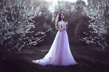 Çiçeklenme tree yakınındaki pembe elbiseli uzun saçlı güzel romantik kız.
