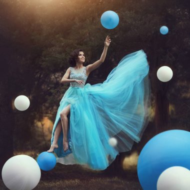 Kadın havalanır. Balonlar ile birlikte mavi kabarık elbise Leets güzel bir kız. Dinamik sanat fotoğraf. Fantezi ve Sürrealizm. Kız gibi bir peri masalında uçar. Mutlu kız balo ile hel