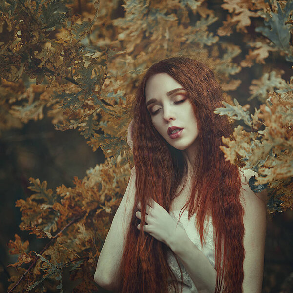Portrait of a beautiful young sensual woman with very long red hair in autumn oak leaves. Colors of autumn.