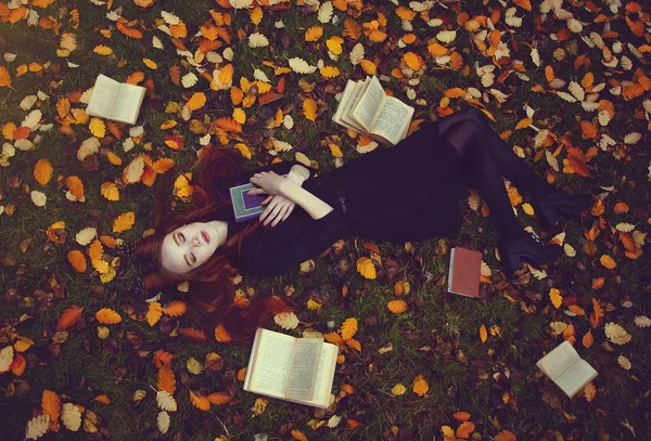 Bella ragazza dai capelli rossi con libri si trova sull'erba in una foresta autunnale, vista dall'alto. Autunno Fotografia da favola . — Foto Stock