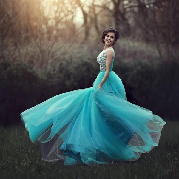 Una bella ragazza laureata sta girando in un vestito blu. Elegante giovane donna in un bellissimo vestito nel parco. Foto d'arte . — Foto Stock