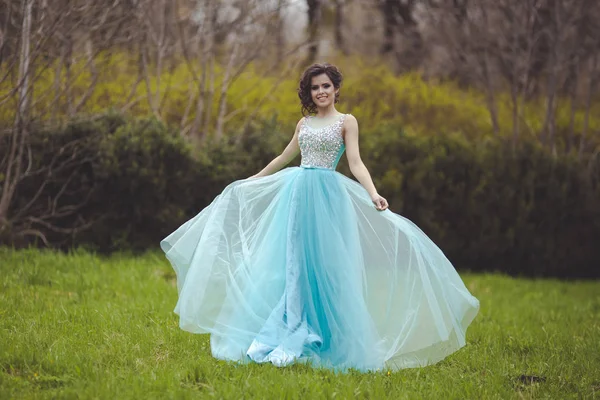 Een mooi afgestudeerde meisje draait in een open plek in een blauwe jurk. Elegante jonge vrouw in een mooie jurk in het park. Kunst foto. — Stockfoto