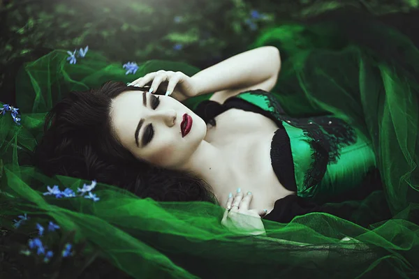 Retrato de mulher misteriosa com flores azuis. Mulher modelo bonita em um vestido verde Face Closeup. Escuridão . — Fotografia de Stock