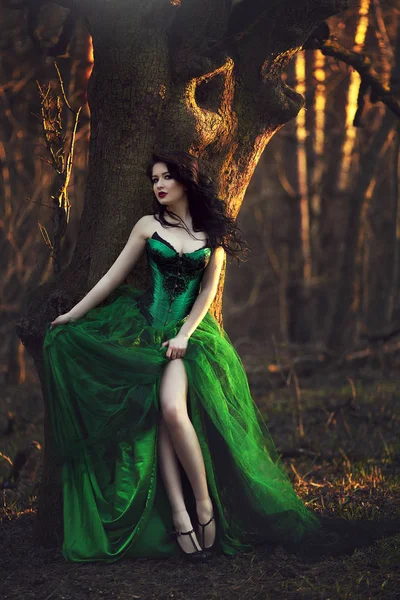 Mädchen in grünem Kleid posiert neben Baum im Wald. — Stockfoto