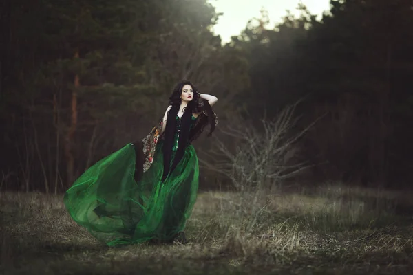 Een meisje in een groene jurk en een sjaal wandelingen door het bos. — Stockfoto
