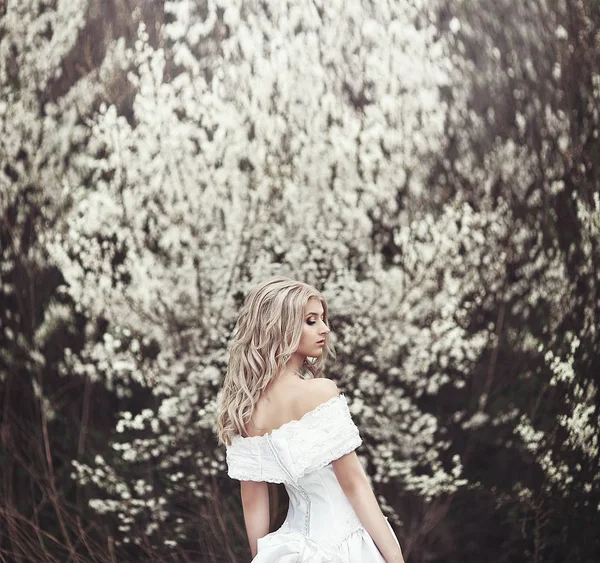 Mooi jong meisje in een mooie witte jurk in de buurt van een bloeiende boom. — Stockfoto