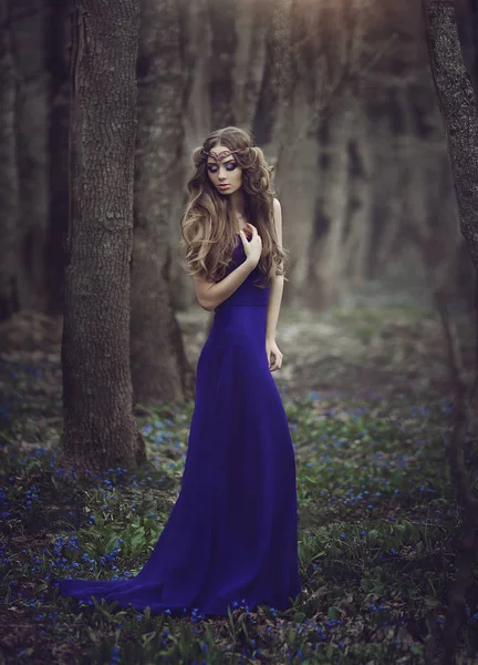 De elf van het meisje met lang haar en blauwe ogen in tiara en een lange blauwe jurk met een trein door het voorjaar bloeiende bos wandelen. Meisje prinses dromen. — Stockfoto