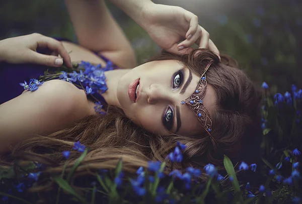 Ragazza elfo con i capelli lunghi e gli occhi azzurri nella tiara riposa nella foresta primavera fiori della foresta blu. Ragazza principessa sogni . — Foto Stock