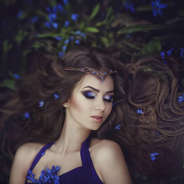 Elf girl with long hair in the tiara rests in spring forest blue forest flowers. Girl Princess dreams. — Stock Photo, Image