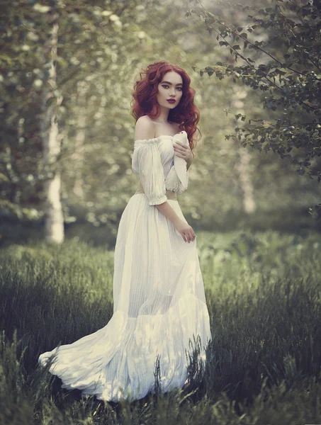 Uma sensual menina ruiva em um vestido branco com ombros nus segura uma pomba branca em sua mão. Pomba branca é um símbolo de paz . — Fotografia de Stock