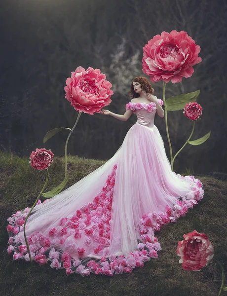 Mooie sensuele meisje met rood haar in een sprookje roze jurk met een enorme trein poseren in de buurt van de gigantische bloemen van een roze pioen. Het meisje is een prinses bloem. — Stockfoto