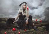 Hexenmädchen mit Hut und schwarzer Katze im Rauch hält rote Kerzen. Sexy Hexe im Wald.