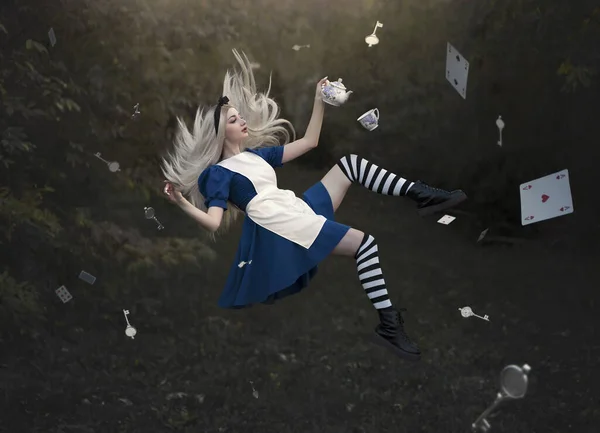 Een mooi blond meisje zweeft met een mok thee boven de grond. Geen zwaartekracht. Zoals Alice in Wonderland. Een meisje met lang haar vliegt als in een sprookje. — Stockfoto