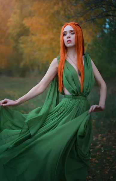 Een prachtig langharig roodharig elfenmeisje staat in de wind in het herfstbos. Een fee vrouw met lang haar in een fee jurk. — Stockfoto