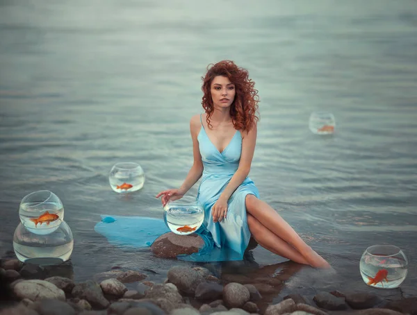 Roodharig meisje op het meer en aquaria met goudvissen. Romantisch beeld van een dromerig meisje in de wind. Surrealisme. — Stockfoto