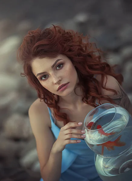 Портрет рыжеволосой девушки на озере и аквариум с золотой рыбкой. Романтический образ мечтательной девушки, загадывающей желание . — стоковое фото