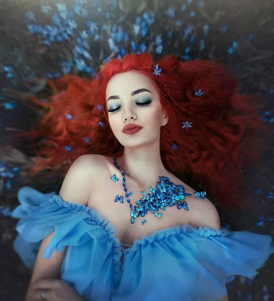 Vlinder meisje in een ketting van blauwe vlinders ligt in het bos in bloemen. Vrouwelijke fee in een sprookjesbos. Art.. — Stockfoto