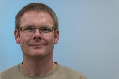 Mavi arka plan önünde gülümseyen adam