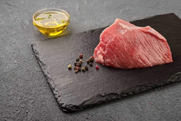 Raw  beef steak on a dark  board. Fresh raw meat with spices and oil.