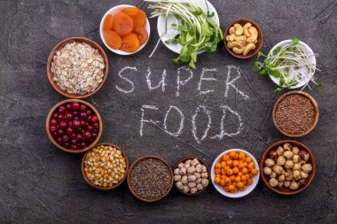 Farklı süper yiyecekler, tohumlar, fındıklar, tahıllar, kızılcıklar, kurutulmuş kayısılar, deniz dikenleri, yabanmersinleri, yulaf ezmesi, mikro yeşiller. Vejetaryen sağlıklı beslenme konsepti. Üst görünüm