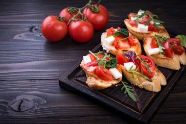 İçinde domates, mozzarella peyniri ve siyah arka planda kesim tahtası olan otlar.