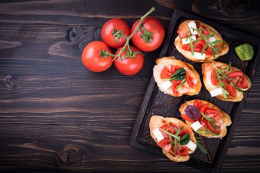 İçinde domates, mozzarella peyniri ve siyah arka planda kesim tahtası olan otlar var.