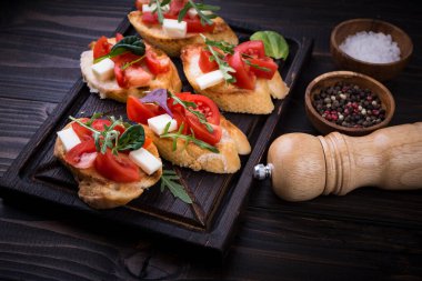 İçinde domates, mozzarella peyniri ve siyah arka planda kesim tahtası olan otlar.