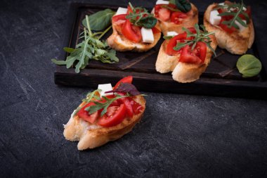 İçinde domates, mozzarella peyniri ve siyah arka planda kesim tahtası olan otlar.