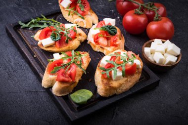 İçinde domates, mozzarella peyniri ve siyah arka planda kesim tahtası olan otlar.