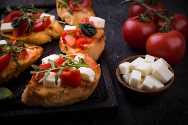 İçinde domates, mozzarella peyniri ve siyah arka planda kesim tahtası olan otlar.