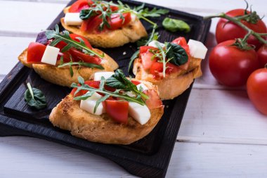 Beyaz arka planda domates, mozzarella peyniri ve kesim tahtasının üzerinde otlar.