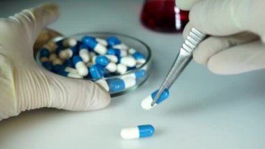 Doktor yeni bir ilaçla birlikte cımbızla bir kapsül alır ve ona aktarır. Konsept - uyuşturucu testi, uyuşturucu kalite kontrolü