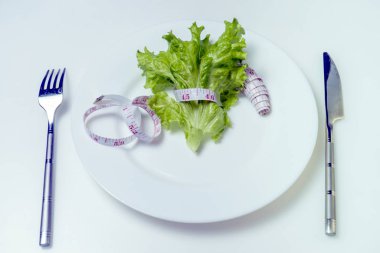 Diyet konsepti. Beyaz tabakta yeşil salata ve mezura..