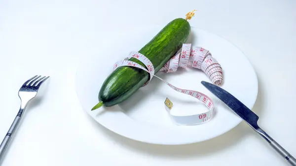 Il concetto di dieta e stile di vita sano. Vista dall'alto di un piatto in cui giace un cetriolo, legato con un metro, con una forchetta e un coltello, è sul tavolo. . — Foto Stock