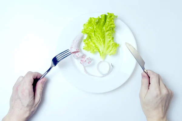 Il concetto di dieta. Le mani maschili tengono una forchetta e un coltello sopra un piatto con insalata verde con un metro . — Foto Stock