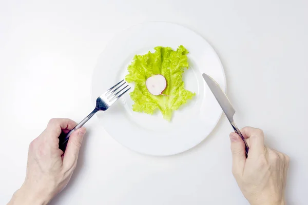 Il concetto di dieta. Le mani maschili tengono una forchetta e un coltello sopra un piatto con insalata verde e ravanello . — Foto Stock