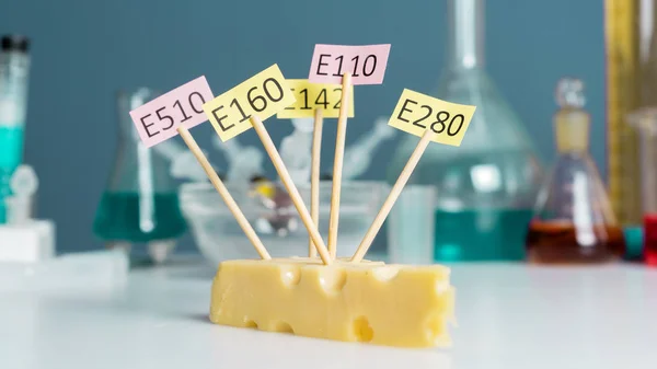E katkı maddeleri ile süslenmiş bir chees, test tüpleri yakında duruyor. Yemek laboratuarı. Beyaz bir masaya yakın..