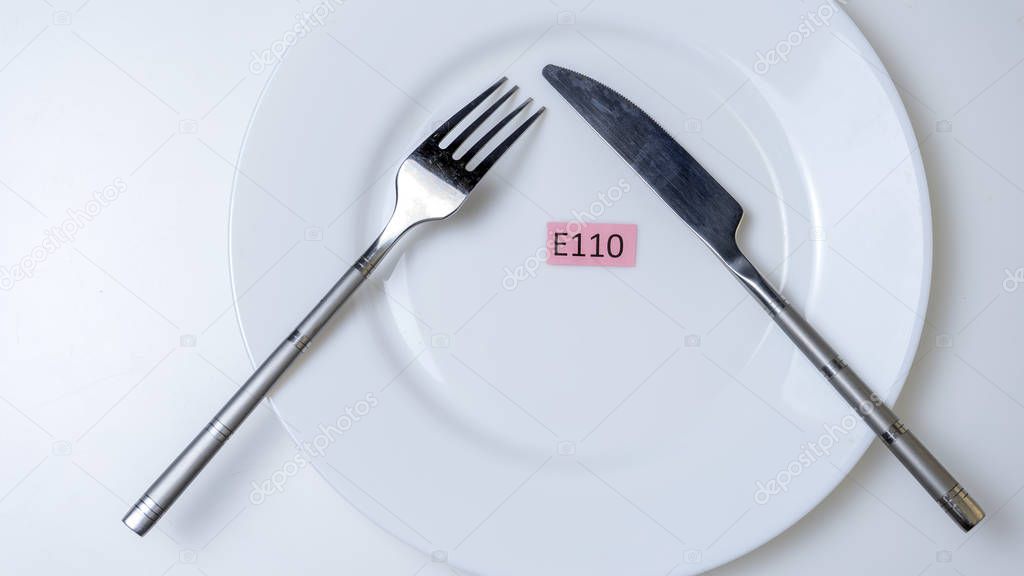 Harmful food additives. Knives, fork, plate. On the plate there are several table with the E-supplement code.