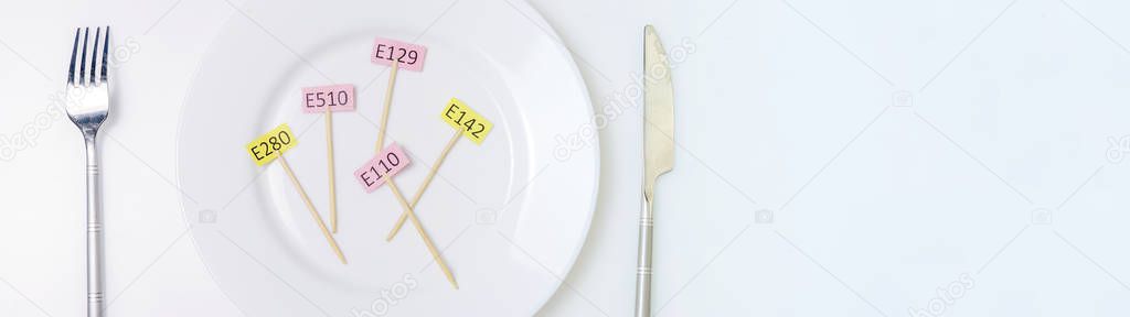 Harmful food additives. Knives, fork, plate. On the plate there are several tables with the E-supplement code. Copy space